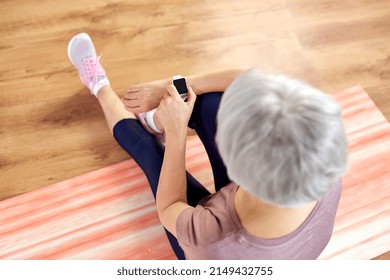 sport, fitness and healthy lifestyle concept - smiling senior woman with smart watch or tracker exercising at home