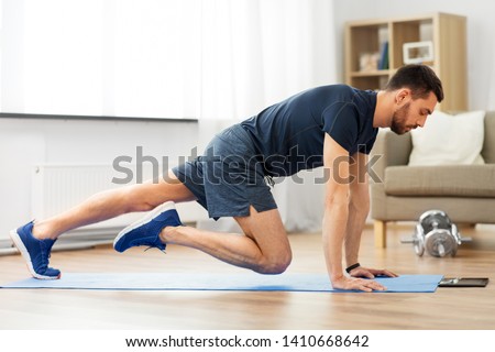 sport, fitness and healthy lifestyle concept - man with tablet computer doing running plank exercise at home