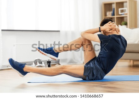 sport, fitness and healthy lifestyle concept - man making bicycle crunch on exercise mat and flexing abs at home