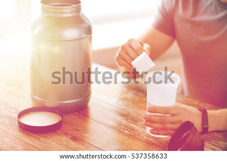 sport, fitness, healthy lifestyle and people concept - close up of man in fitness bracelet with jar and bottle preparing protein shake 商業照片 © 