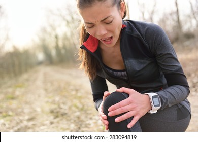 Sport And Fitness Injury - Female Runner With Hurting Knee. Running Woman Screaming In Pain During Run Wearing A Smartwatch. Painful Joint During Workout.