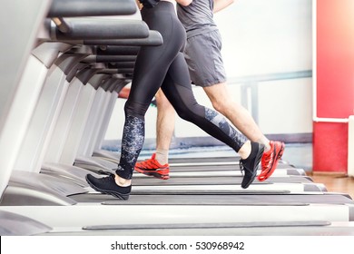 Sport-, Fitness-, Lifestyle-, Technologie- und People-Konzept - Nahaufnahme von Beinen von Frauen und Männern, die im Fitnessraum auf Laufbändern laufen.