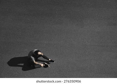Sport fitness man relaxing after training. Young male athlete resting sitting in asphalt after running and training exercise outside in summer. Caucasian man sports model.