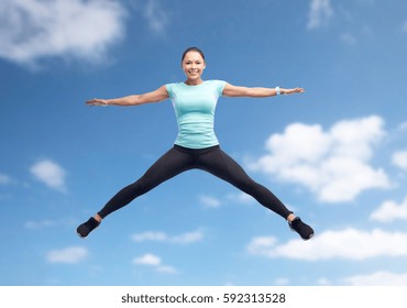 sport, fitness, motion and people concept - happy smiling young woman jumping in air over blue sky and clouds background - Shutterstock ID 592313528