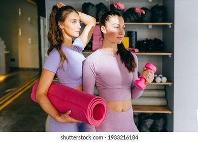 Sport, Fitness, People And Friendship Concept. Two Happy Smiling Young Sporty Women Best Friends Tied In Pony Tail With Light Pink Dumbbells Over Gym On Background.