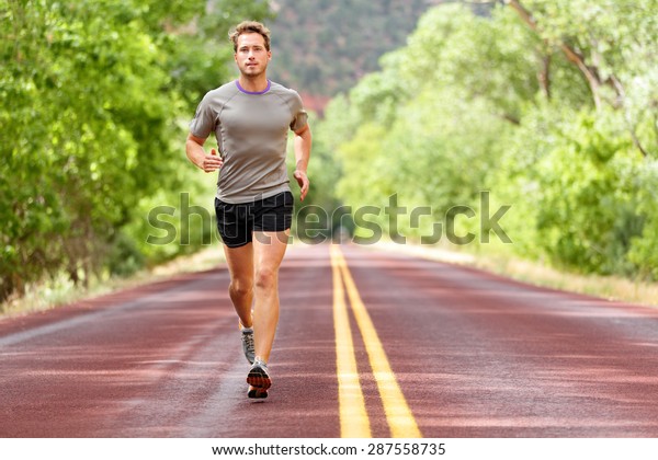 Sport and fitness runner man running on road\
training for marathon run doing high intensity interval training\
sprint workout outdoors in summer. Male athlete sports model fit\
and healthy aspirations.