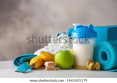 Sport food and  equipment- shaker with a protein, protein bar, banana, apple, mat, gym shoes, block,  belt . Fitness or yoga concept. Copy space
