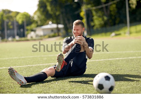 sport, football training, sports injury and people - injured soccer player with ball on field