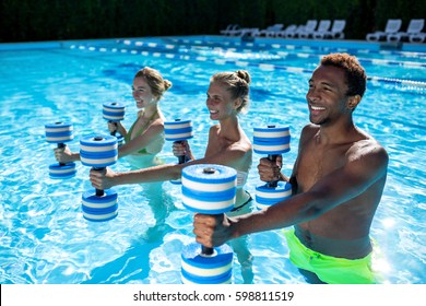 Sport with friends at resort. Group of  sportive young people doing aqua fitness exercise with plastic dumbbells in swimming pool on summer sunny day outdoors