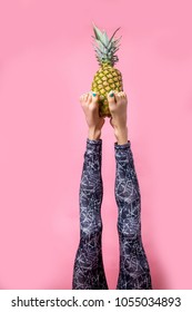 Sport girl doing yoga stretching - sirsasana, headstand. Legs of yoga girl holding pineapple while practicing over vibrant background
