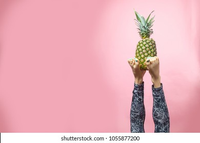 Sport girl doing yoga stretching - sirsasana, headstand. Legs of yoga girl holding pineapple while practicing over vibrant background