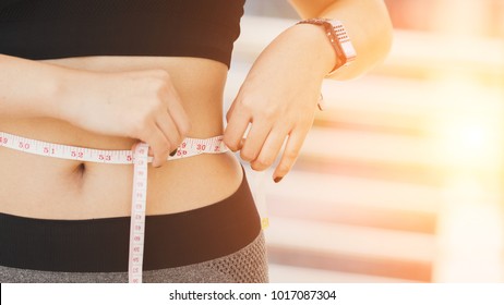 Sport girl measuring waist with yellow measuring tape, reducing excess weight. Healthy lifestyle.