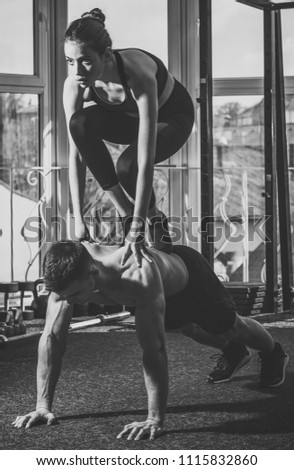 Sport and gym concept. Man and woman in sportswear in gym, window on background. Couple does acroyoga, physical practice of yoga and acrobatics. Athletes muscular and strong practicing acroyoga at gym