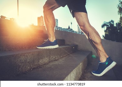Sport hard. Close up of male feet climbing stairs outside. Well shaped man is jogging at dawn