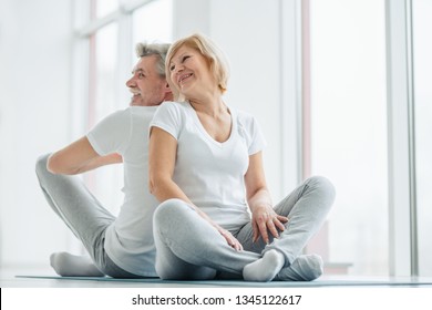 Sport and health concept.Senior couple sitting on the mat back to back laughing and talking. Leisure time in the training.