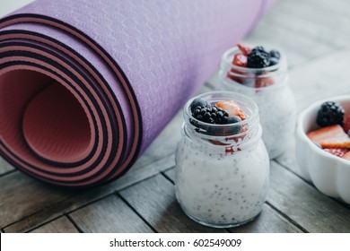 Sport and healthy concept. Pink yoga mat and Pudding with chia seeds, yogurt and fresh fruits: Strawberries, blueberries and blackberries in glass jars on wooden background