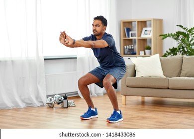 sport and healthy lifestyle concept - indian man with fitness tracker exercising and doing squats at home - Powered by Shutterstock