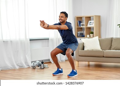 Sport And Healthy Lifestyle Concept - Smiling Indian Man With Fitness Tracker Exercising And Doing Squats At Home