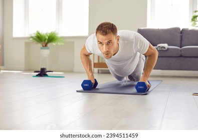 Deporte, estilo de vida saludable, buen estado corporal y salud de los hombres. Retrato de deportistas serios que practican deportes en casa y entrenan músculos usando dumbombs. El hombre hace 'push-ups' en el suelo en la sala de estar.