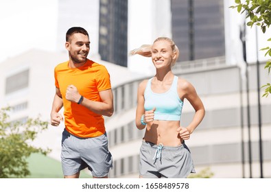 Sport, Healthy Lifestyle And People Concept - Smiling Couple With Fitness Trackers Running At Summer Over City Street On Background