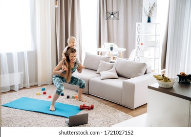 Sport At Home. Young Attractive Mom Doing Sports At Home And Watching A Video Fitness Lesson On A Laptop, With Her Little Baby Girl