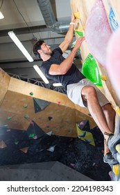 Sport Ideas. Rock Climber Man Hanging On A Bouldering Climbing Wall, Inside On Colored Hooks.Vertical Shot