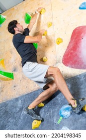 Sport Ideas. Rock Climber Man Hanging On A Bouldering Climbing Wall, Inside On Colored Hooks.Vertical Image