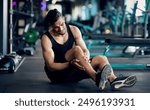 Sport Injury. Upset Arab Male Athlete Suffering From Knee Trauma While Training At Gym, Middle Eastern Man Sitting On Floor And Massaging Aching Area, Sporty Guy Frowning With Pain, Copy Space