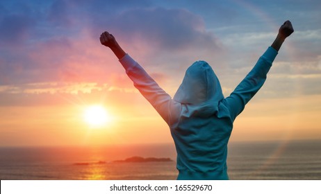 Sport and life achievements and success concept. Rear view sporty girl raising arms towards beautiful glowing sunshine.