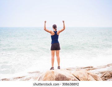 Sport and life achievements and success concept. Rear view sporty girl raising arms towards the sea, Thailand
