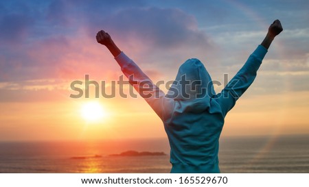 Sport and life achievements and success concept. Rear view sporty girl raising arms towards beautiful glowing sunshine.
