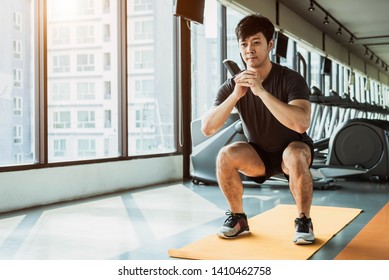 Sport Man Doing Squat Posture On Yoga Mat In Fitness Gym At Condominium In Urban. People Lifestyles And Sport Workout Concept.