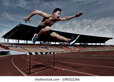 The Sport Man  To Runner Jumping Over An Hurdle During Track And Field Event. Athlete Running A Hurdle Race In A Stadium.Dramatic Image