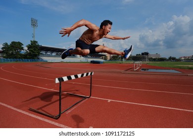 The Sport man to runner jumping over an hurdle during track and field event. Athlete running a hurdle race in a stadium.Dramatic image - Shutterstock ID 1091172125