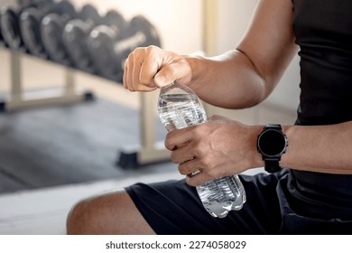 Sport man with well trained body in black sportswear opening water bottle while sitting on workout bench in fitness gym. Drinking water after weight training exercise. - Powered by Shutterstock