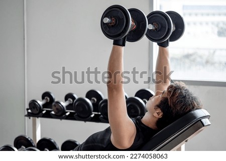 Sport man with well trained body in black sportswear doing incline dumbbell shoulder press on workout bench in fitness gym. Weight training and bodybuilding workout concept.
