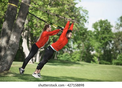 Sport Man And Woman Training With Suspension Trainer Sling Or Trx In Park. Man As Personal Trainer Showing His Partner How To Keep Fit.