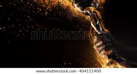 Sport. Man's hand holding up trophy goblet. Winner in a competition. Fire and energy