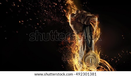 Sport. Man's hand holding up trophy medal. Winner in a competition. Fire and energy