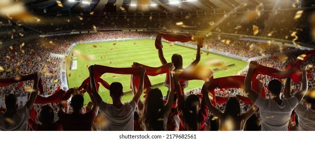 Sport match. Back view of football, soccer fans cheering their team with colorful scarfs at crowded stadium at evening time. Concept of sport, cup, world, team, event, competition