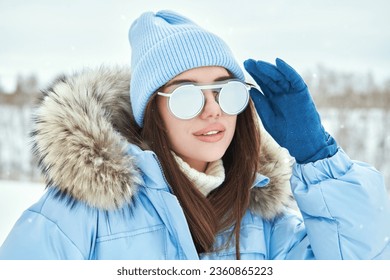Sport in the mountains. Winter fashion. Portrait of a fashionable girl posing in blue ski suit against a snowy winter landscape.