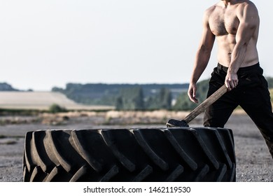 Sport Muscular Man Hitting Wheel Tire With Hammer Sledge In The Gym. Sports Training