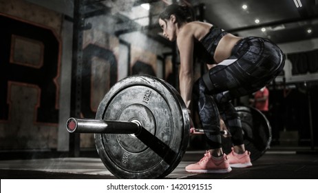 Sport. Muscular women lifting deadlift in the gym with barbell. Dramatic interior with smoke.