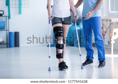 Sport physiotherapist and patient with leg injury during training with crutches
