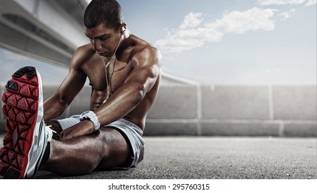 Sport. Runner. Muscular young african man looking away with stretching his leg. 