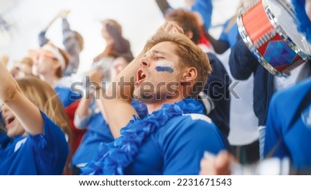 Sport Stadium Big Event: Handsome Happy Caucasian Man Emotionally Cheers, Screams. Crowd of Fans with Painted Faces Celebrate Championship Victor, their Blue Soccer Team is Winning.