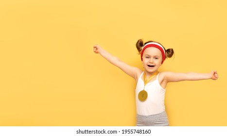 Sport Success And Win Concept - Smiling And Happy Athlete Champion Child Girl Celebrates First Place Victory Gold Medal Award. Sport Kid Posing Over Yellow Studio Background. Banner, Mockup,copy Space