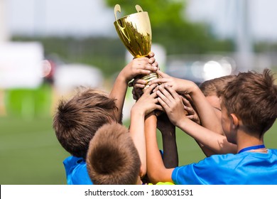 Sport Team Celebrate Success. Happy Boys Rising Golden Cup On Celebration. Kids Winning Sports School Tournament Competition. Inter-school Sport Competition. Kids In Blue Sport Shirts