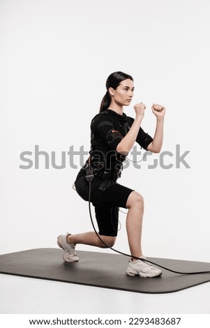 Sport training in EMS electrical muscle stimulation suit. Fitness girl in EMS suit is doing workout sport training that uses electrical impulses to stimulate muscles on white background