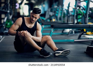 Sport Trauma. Young Arab Male Athlete Touching His Hurted Knee At Gym, Upset Middle Eastern Guy Sitting On Floor And Massaging Sore Injured Leg After Workout Training In Fitness Club, Free Space - Shutterstock ID 2114910554